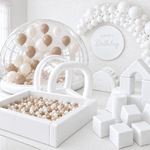 White bubble bounce with balloons beside an all-white soft play setup