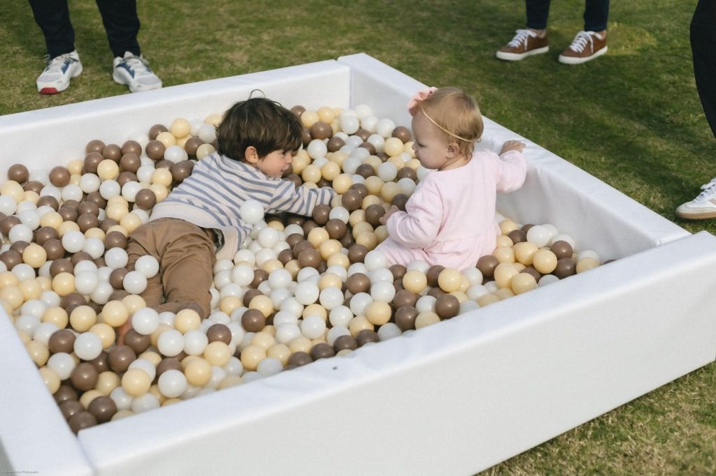 Two little ones playing in the white ball pit with mocha, cream and white balls