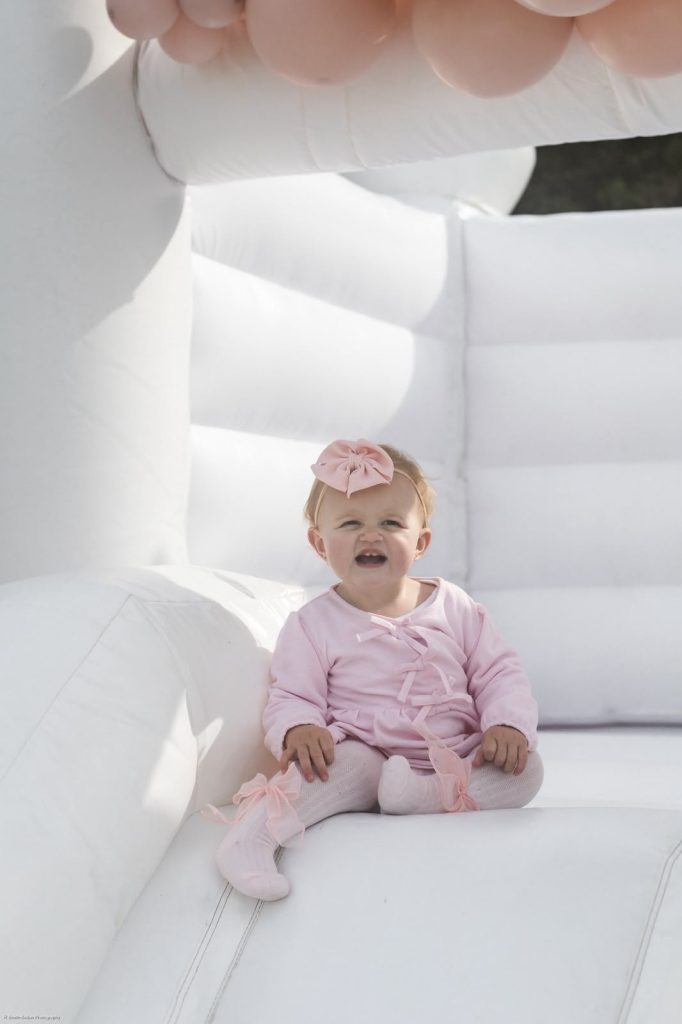 Baby sitting inside the white jumping castle under blush balloons